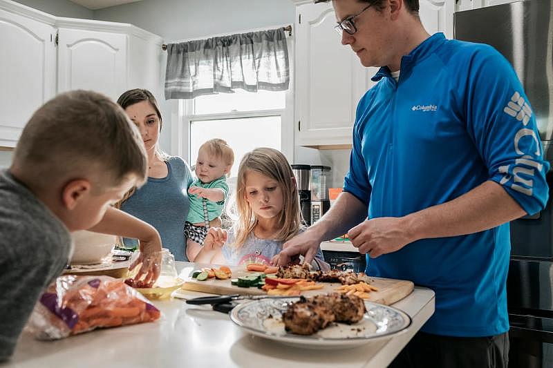 Ann watches her father prepare dinner at home with other members of their family.